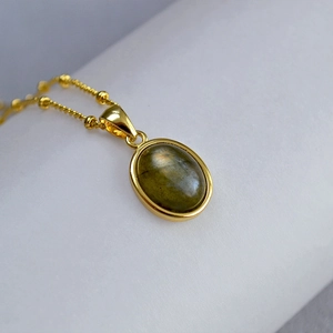 Macro shot of oval labradorite pendant with golden beaded chain and polished finish