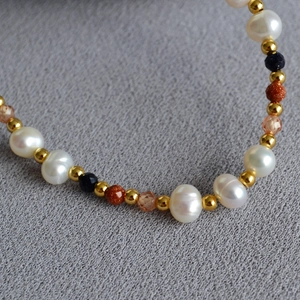Macro detail of Baroque pearls with blue sandstone and gold beads on a textured surface