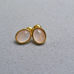 Detailed close-up of gold-plated oval stud earrings with smooth pink natural stone