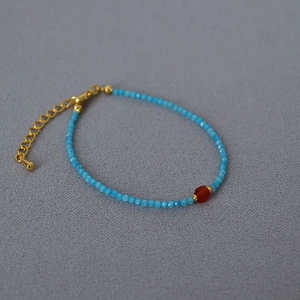 Minimalist light blue faceted gemstone beaded bracelet with a red center stone and gold clasp
