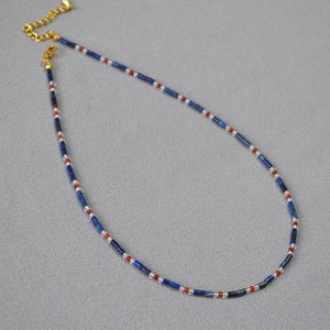 Detail of beaded necklace with blue lapis lazuli and red beads with a gold lobster clasp