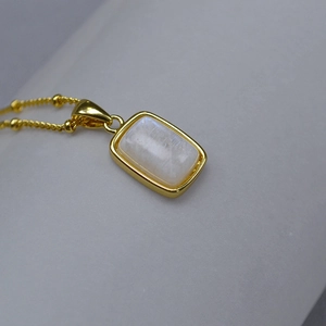Detail of a rectangular moonstone pendant on a gold beaded chain with elegant metal edges