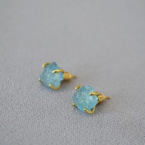 Detail view of irregular natural blue gemstone earrings with four-prong gold-plated settings