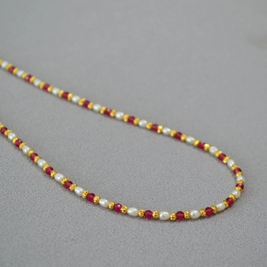 Close-up of elegant beaded necklace with red corundum and rice pearls on grey fabric