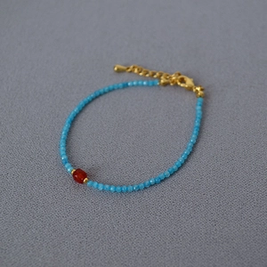 Close-up of blue faceted stone beads with red agate accent and gold-plated lobster clasp