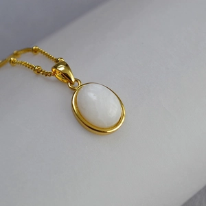 Macro view of gold oval pendant with inlaid white stone on delicate beaded chain