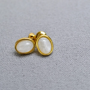 Detailed macro view of gold-plated oval stud earrings with white natural stone inlay