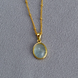 Minimalist gold necklace with oval gemstone pendant and beaded chain for elegant layering