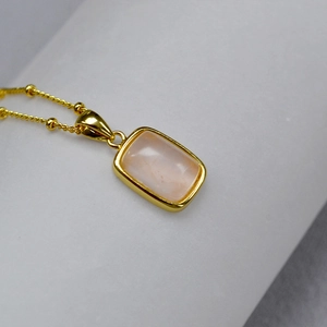 Macro shot of rectangular pink gemstone pendant with gold plated bezel on a beaded chain