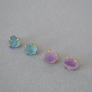 Detailed macro view of raw aquamarine and amethyst stones set in four-prong gold-plated studs