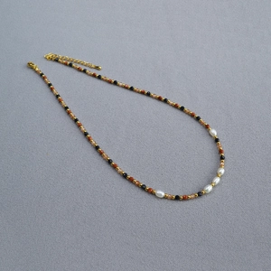 Detail of baroque pearl necklace with gold beads and lobster clasp on grey fabric
