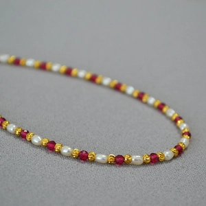 Macro detail of French style pearl necklace with red corundum beads and golden accents
