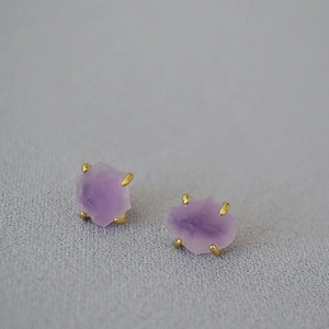 Macro detail of raw amethyst gemstones set in four-prong gold plated brass earrings
