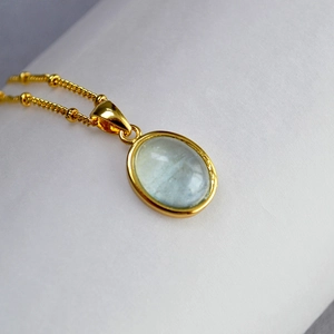 Close-up of a minimalist gold necklace with light blue oval stone and gold bead accents