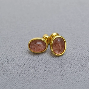 Macro detail of brass gold plated oval stud earrings with natural strawberry quartz stones