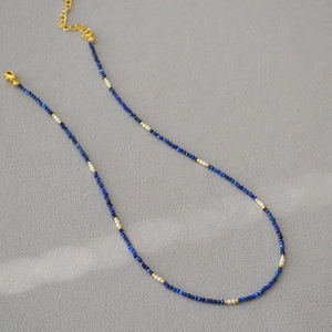 Lapis lazuli and pearl beaded necklace with gold spacers on minimalist grey background