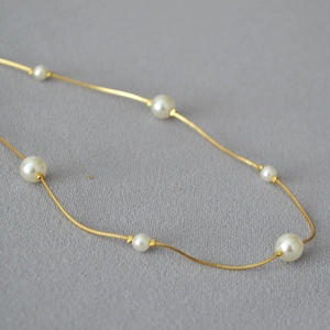 Close-up of elegant gold snake chain necklace with polished white pearls detail