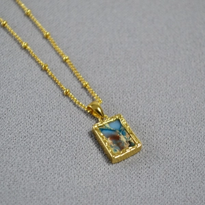 Macro detail of rectangle gold necklace with marble stone and textured border