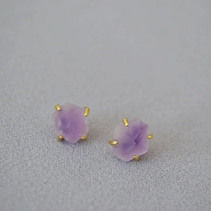 Macro detail of raw purple amethyst stud earrings with four-prong gold plated setting
