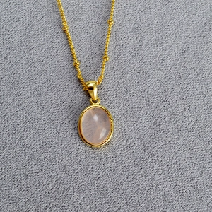 Detail of oval pink stone pendant on a gold beaded chain with elegant polished finish