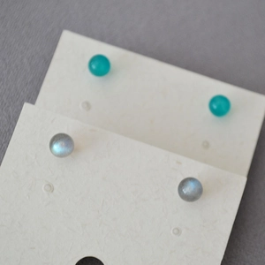 Close-up of small round amazonite and labradorite stud earrings on a card display