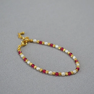Detail of beaded necklace featuring white pearls, red gemstones, and gold spacer beads