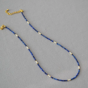 Macro shot of lapis beads, small pearls, and gold clasp on minimalist beaded necklace