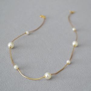 Close-up of gold snake chain necklace featuring alternating white round pearls on grey texture