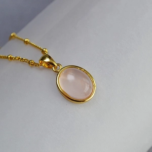 Macro shot of oval gold pendant with pink rose quartz stone and fine textured edge detail