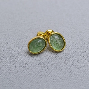 Macro view of gold-plated oval stud earrings with translucent green natural stone