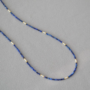 Detail of Lapis Lazuli necklace with white pearls and gold beads on grey texture