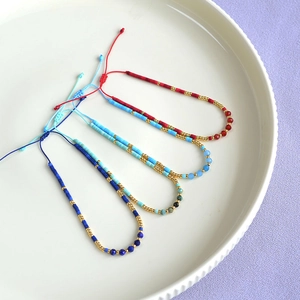 Detail of four colorful bohemian beaded bracelets with adjustable braided ropes on a white tray
