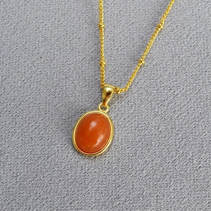 Detailed macro view of an oval orange gemstone pendant on a gold beaded chain necklace