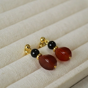 Macro detail of retro red agate drop earrings on a beige velvet jewelry display