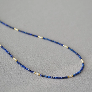 Vintage lapis lazuli and pearl beaded necklace with gold accents on a textured grey background