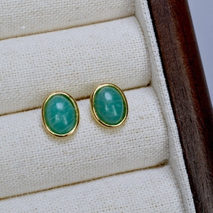 Detail of oval green natural stone earrings with gold plating in a jewelry box