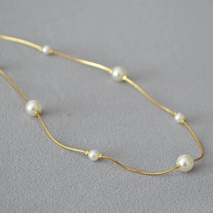 Close-up of golden snake chain necklace with white pearls on dark grey fabric