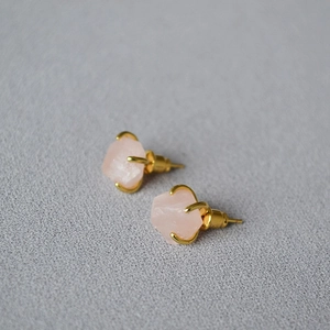 Macro shot of pink raw gemstones set in gold-plated four-claw stud earrings