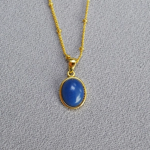 Detailed close-up of a gold necklace with a smooth oval blue gemstone and small gold beads