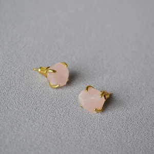 Close-up of pink raw gemstones set in gold-plated four-prong studs on fabric