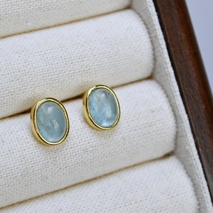 Macro view of oval light blue gemstone earrings with gold-plated bezel settings