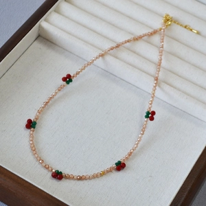 Detail of sweet beaded necklace with champagne zircons and red cherry charms on beige velvet