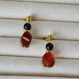 Macro shot of 925 silver stud earrings with red agate beads on a beige texture display