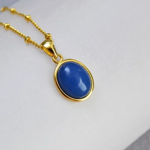 Detail of oval blue natural stone pendant on gold beaded chain necklace