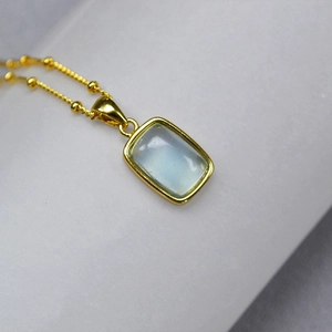 Macro shot of rectangular blue gemstone pendant on a gold beaded chain necklace