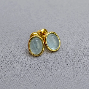 Macro view of gold-plated oval stud earrings featuring light blue natural stone in bezel setting