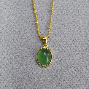 Close-up of golden satellite chain necklace with green oval gemstone pendant