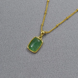 Detail of a vintage geometric green stone pendant on a gold beaded necklace chain