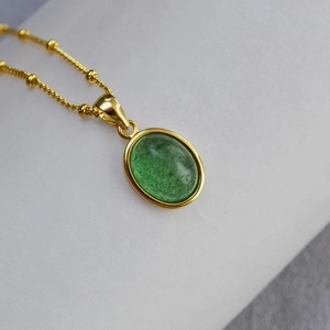 Close-up of oval green stone pendant with polished gold trim on a bead chain necklace