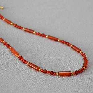 Vintage red agate beaded necklace with gold spacers on a grey fabric background